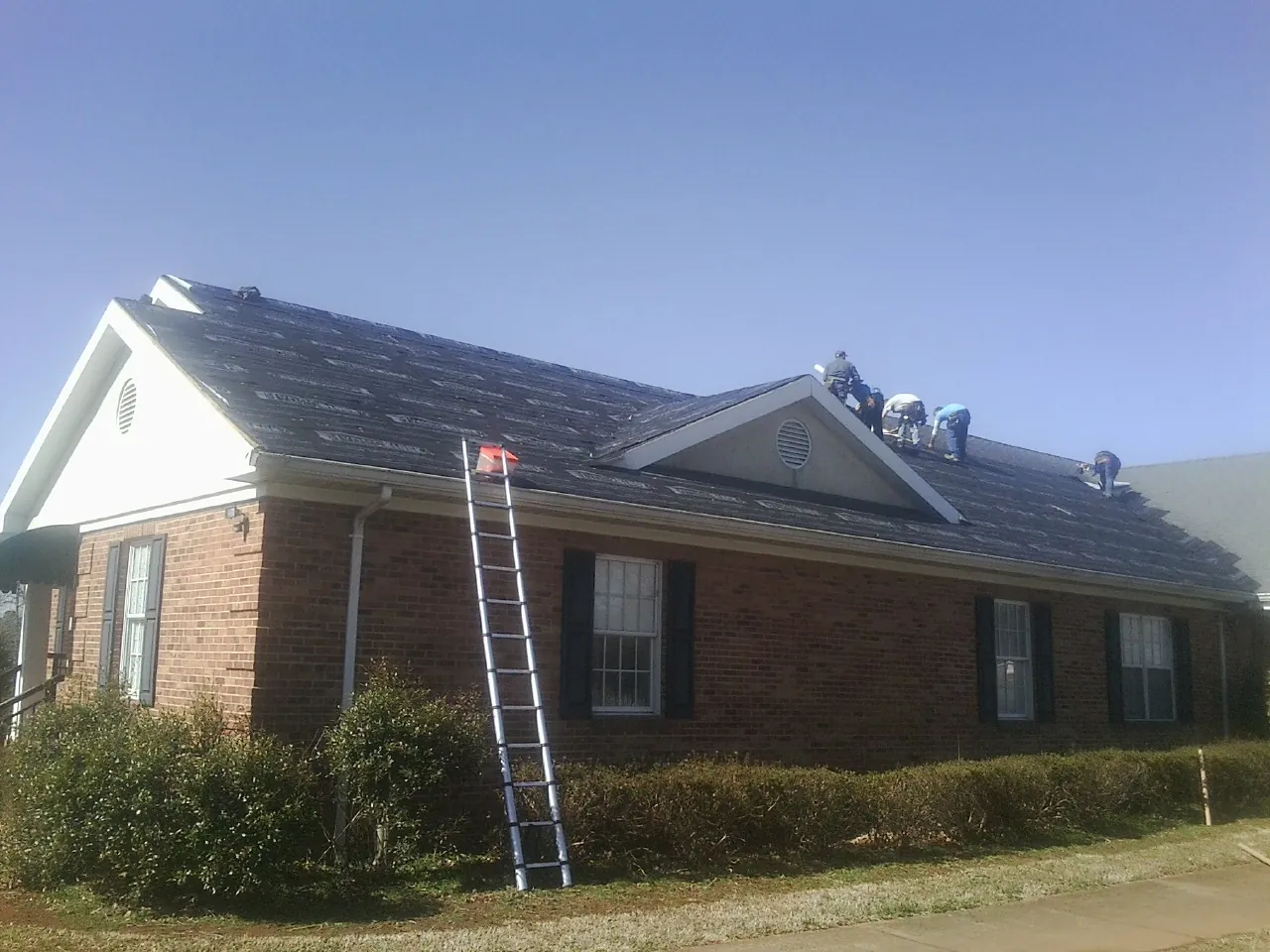 Crew tearing shingles off a brick ranch roof with a ladder set — Metal Roof Repair work by our crew in Chaska