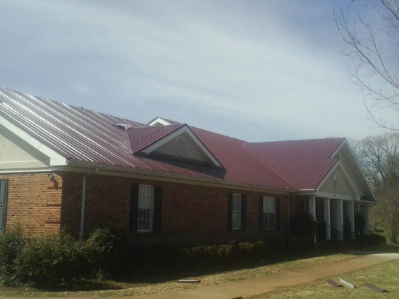 Red metal roof with gabled entries on a long brick building, from a Hail Damage Roof Repair job in Chaska
