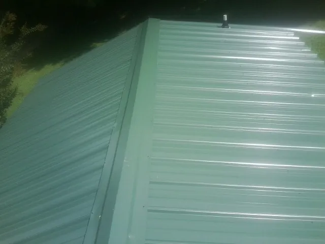 New green metal panels meeting at the ridge of a roof — Flat Roof Repair work by our crew in Chaska
