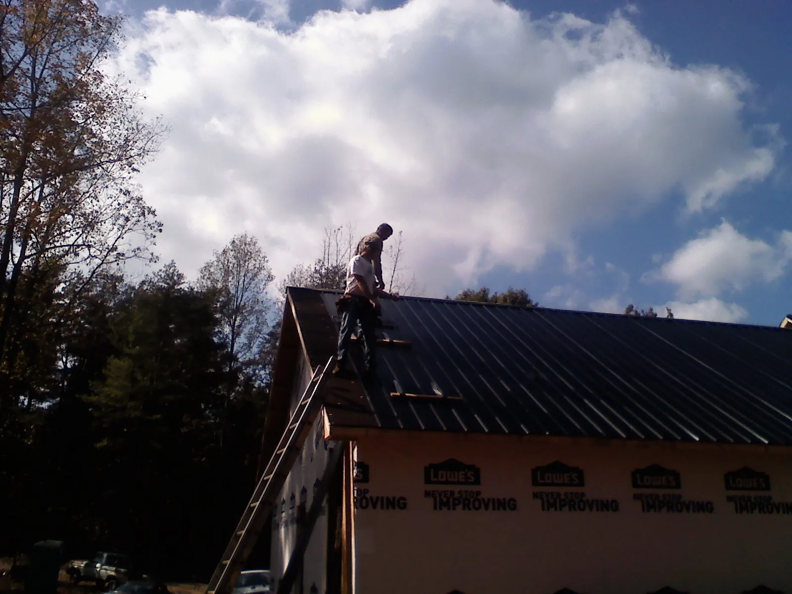 Roofer fastening dark metal panels high against a cloudy sky, from a Roof Inspection job in Chaska