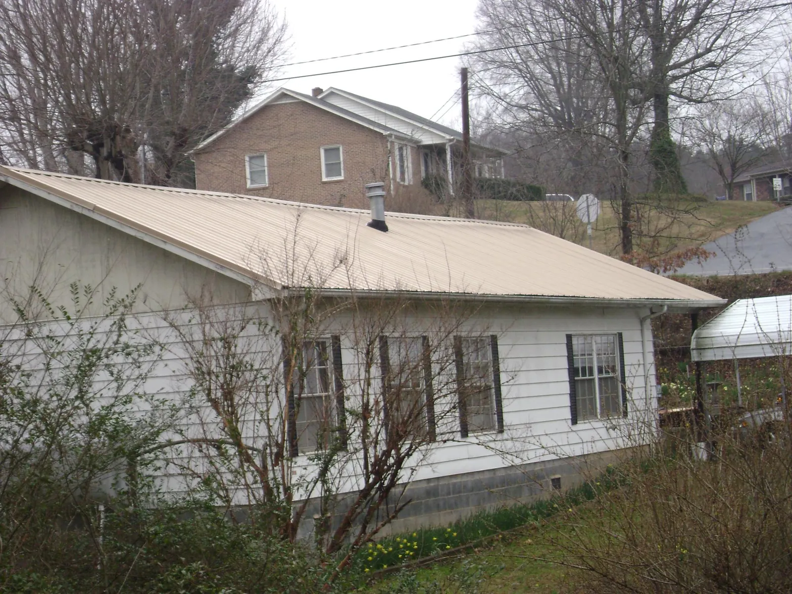 Tan metal roof on a white sided house set into a hillside — Commercial Roofing by Roofing Brothers in Chaska
